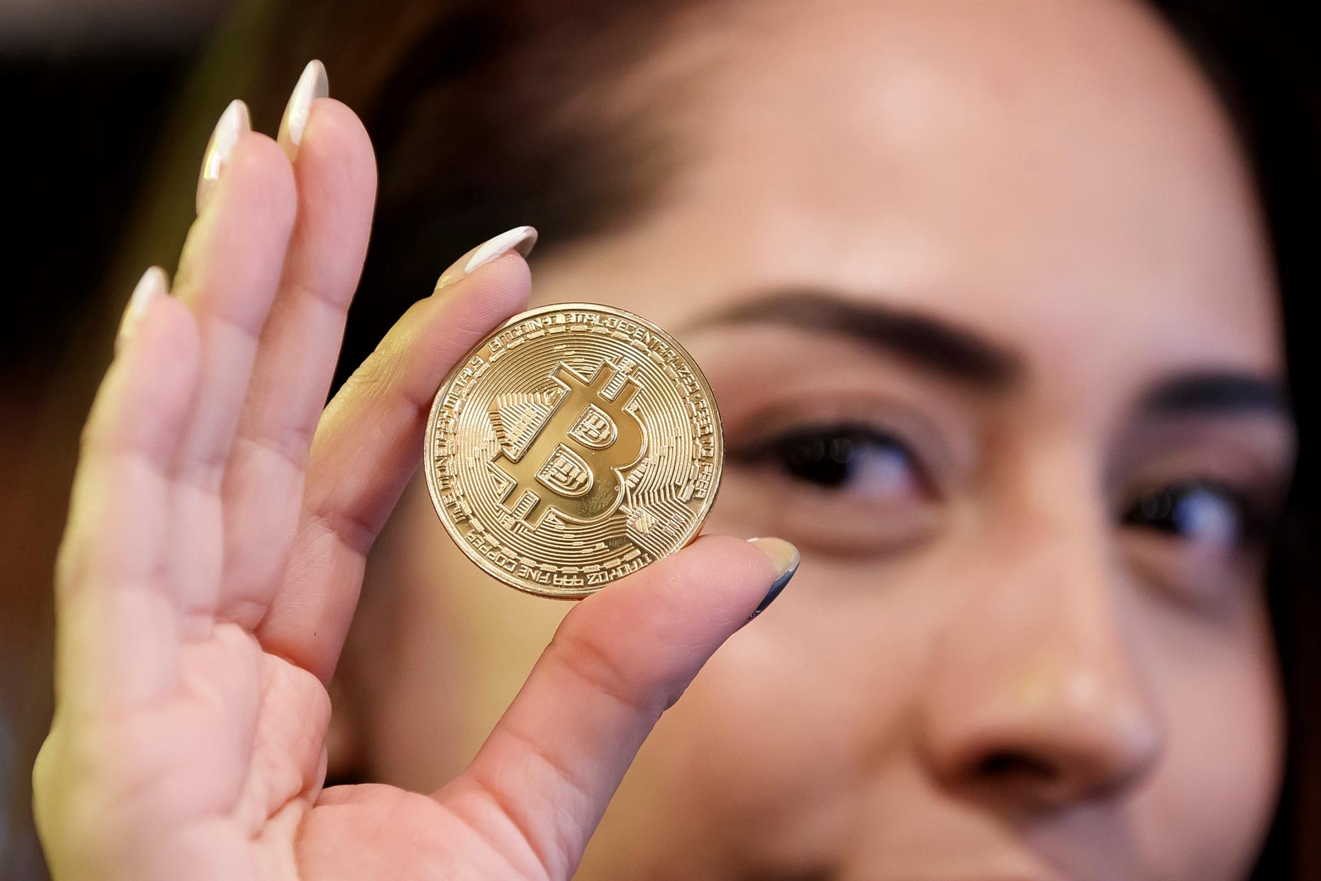 Imagen de archivo que muestra a una mujer mostrando una moneda bitcoin. EFE/José Méndez
