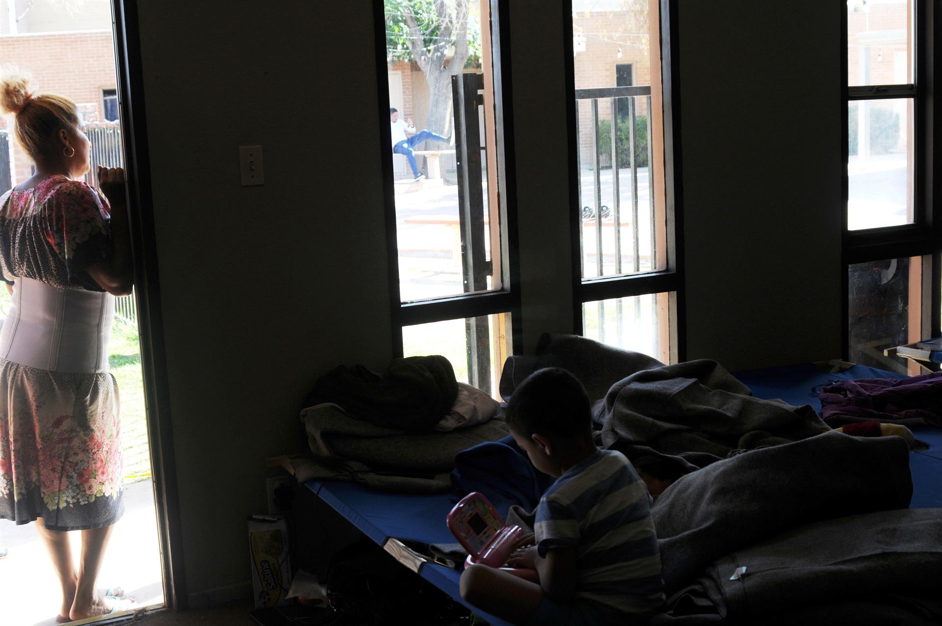 Fotografía donde aparece la inmigrante cubana Maylin mirando desde la puerta de la habitación mientras un niño juega sobre una cama en la iglesia Monte Vista en Phoenix, Arizona. Imagen de archivo. EFE/Beatriz Limón
