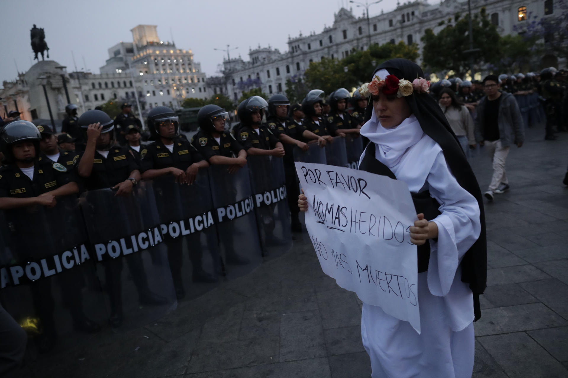 Una mujer con un cartel con un mensaje de paz camina frente a policías en la Plaza de San Martín, donde confluyeron manifestantes opositores al Gobierno y simpatizante a este durante la denominada 