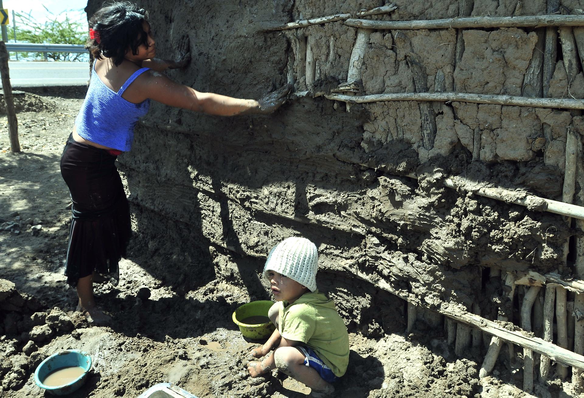 Fotografía de archivo de un niño y una joven que ayudan a construir una pared de lodo. EFE/Gustavo Amador
