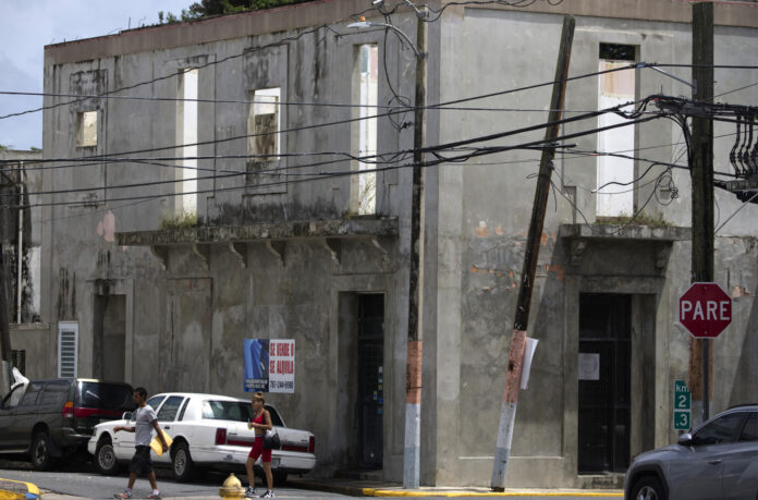 Fotografía que muestra a varias personas mientras caminan frente a un edificio afectado en el 2017 por el paso del huracán María, en el centro del pueblo de Yabucoa (Puerto Rico). Imagen de archivo. EFE/ Thais Llorca
