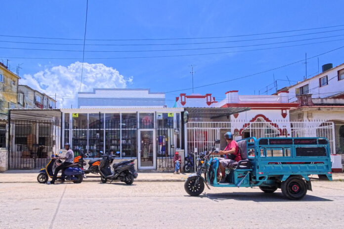 Personas transitan en motos eléctricas frente a un mercado privado este martes, en La Habana (Cuba). EFE/ Ernesto Mastrascusa
