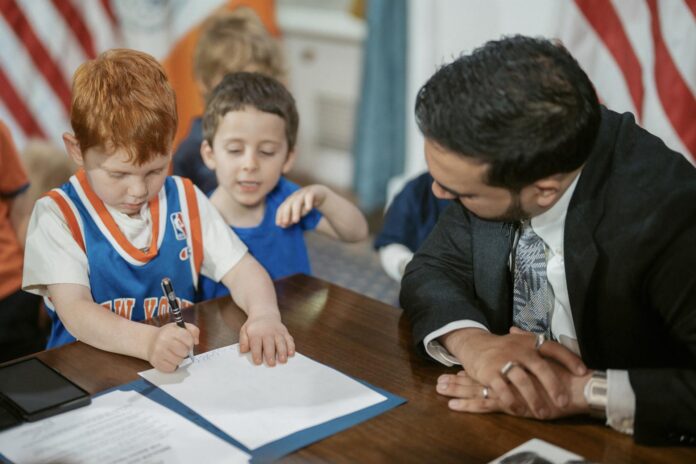Fotografía publicada en la cuenta en X del alcalde de Nueva York, Zohran Mamdani (@NYCMayor) donde aparece junto a unos niños durante la firma de una orden ejecutiva para 
