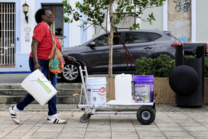 Una mujer transporta baldes de agua tras la interrupción del servicio este lunes, en San Juan (Puerto Rico). EFE/Thais Llorca

