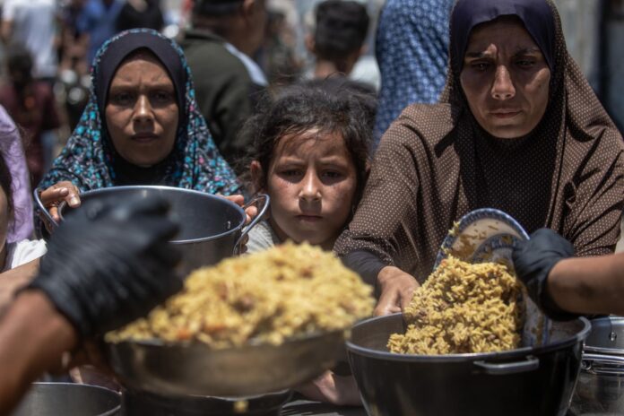 .- Palestinos desplazados sostienen ollas y sartenes de metal mientras se reúnen para recibir comidas calientes de un comedor social en el norte de la ciudad de Gaza, este miércoles. La distribución de alimentos se produjo en medio de una grave escasez de suministros básicos en todo el enclave. Agencias de la ONU informaron que, a pesar de un alto el fuego nominal, la entrada de ayuda vital a Gaza sigue estando muy restringida. EFE/ Mohammed Saber
