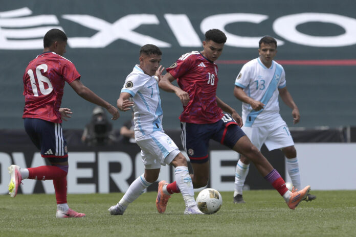 El guatemalteco Yordi Aguilar (c) disputa el balón con el costarricense Dax Palmer (2-d) durante el partido de la primera jornada del torneo sub-20 de la Concacaf, clasificatorio para los Juegos Olímpicos de Los Ángeles 2028 que se jugó este viernes en el estadio Cuauhtémoc en Puebla. EFE/ Hilda Ríos
